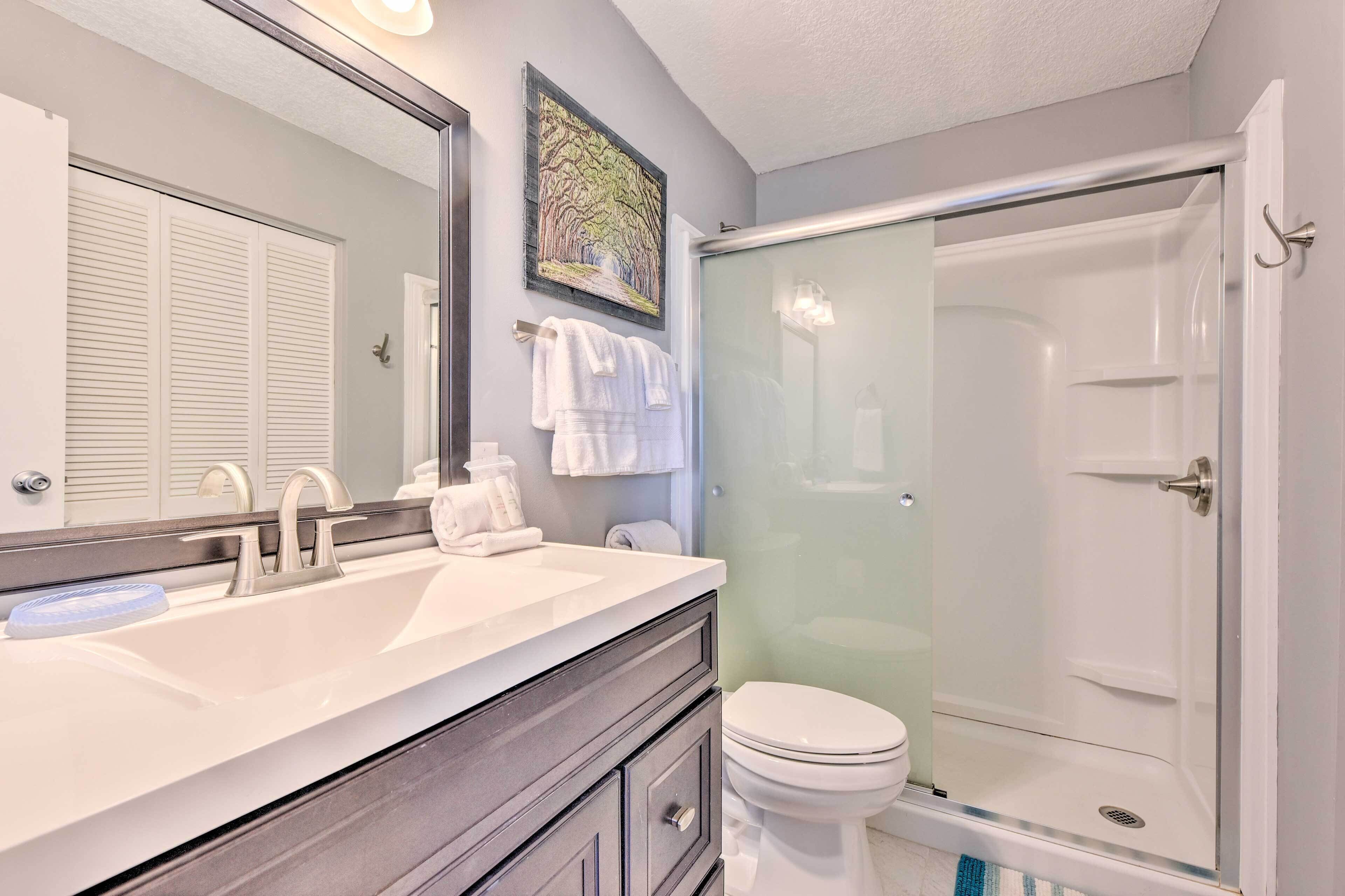 A bathroom with a double sink, a toilet, a glass-enclosed shower, and a towel rack with towels.