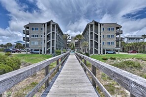Une promenade en bois mène à un immeuble moderne doté de nombreux balcons, avec un ciel dégagé en toile de fond.