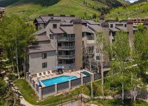 Un hotel de varios pisos con piscina, mobiliario exterior y vistas a las colinas circundantes.