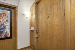 Eine Holztür mit der Nummer 5, einem gerahmten Poster und einer Wandleuchte.