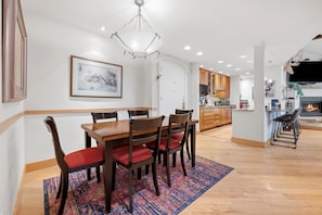 A dining area with a wooden table and chairs, a colorful rug, and a chandelier.
