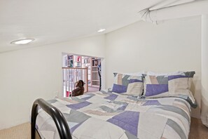 Une chambre à coucher comprenant un lit, une chaise, une bibliothèque et une porte donnant sur une autre pièce.