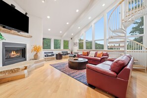A spacious living room with a fireplace, leather sofas, a coffee table, and large windows offering a view of the outdoors. - Luxury Condo in Vail Village, Walk to Lifts, Tyro5 (Vail)