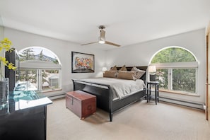 A bedroom with a bed, a desk, a chair, a suitcase, and large windows.