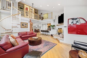 A spacious living area with a red sofa, a coffee table, and a staircase leading to a loft with bookshelves. - Luxury Condo in Vail Village, Walk to Lifts, Tyro5 (Vail)