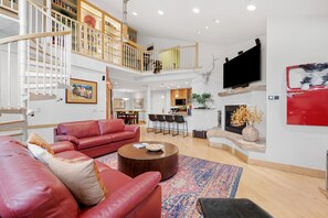A spacious living room with a red leather sofa, a coffee table, and a fireplace. There is a dining area with a table and chairs, and a kitchen in the background. - Luxury Condo in Vail Village, Walk to Lifts, Tyro5 (Vail)