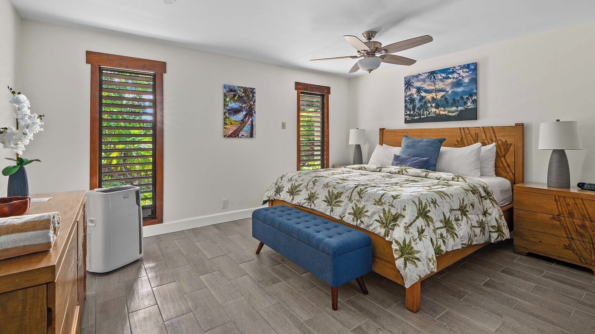 A bedroom with a bed, a bench, a ceiling fan, and two windows with blinds.