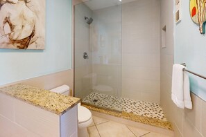 A modern bathroom with a glass shower enclosure, a granite countertop, and a toilet.