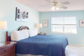 A bedroom with a bed, a ceiling fan, a window with blinds, and wall art.