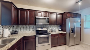 A kitchen with dark wood cabinets, stainless steel appliances, a granite countertop, and a tiled backsplash.
