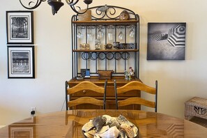 A dining area with a wooden table, chairs, and a decorative shelf with glassware and a rooster figurine.
