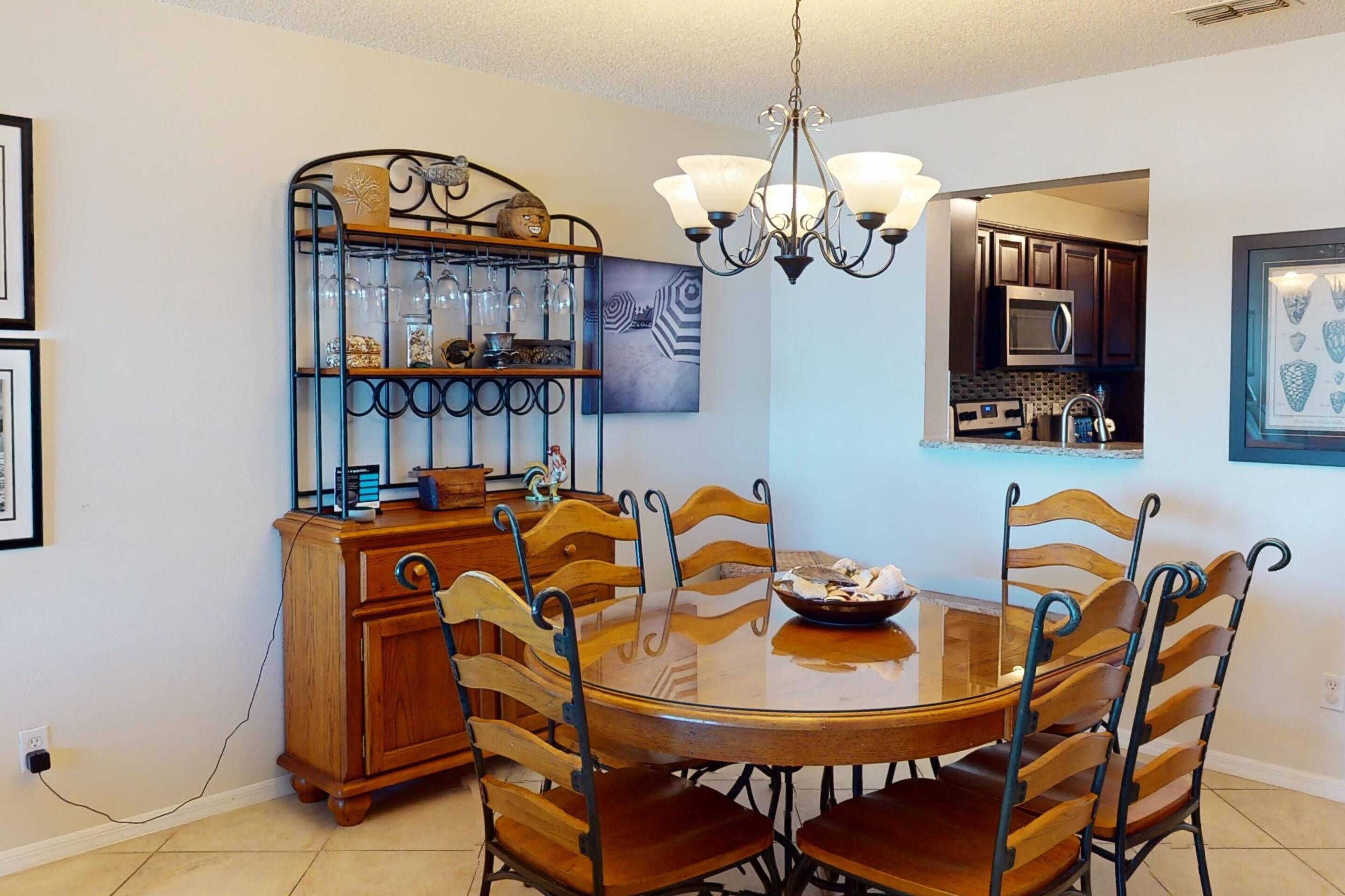 Un comedor con una mesa redonda de madera, seis sillas, una araña, un estante metálico decorativo y un microondas al fondo.