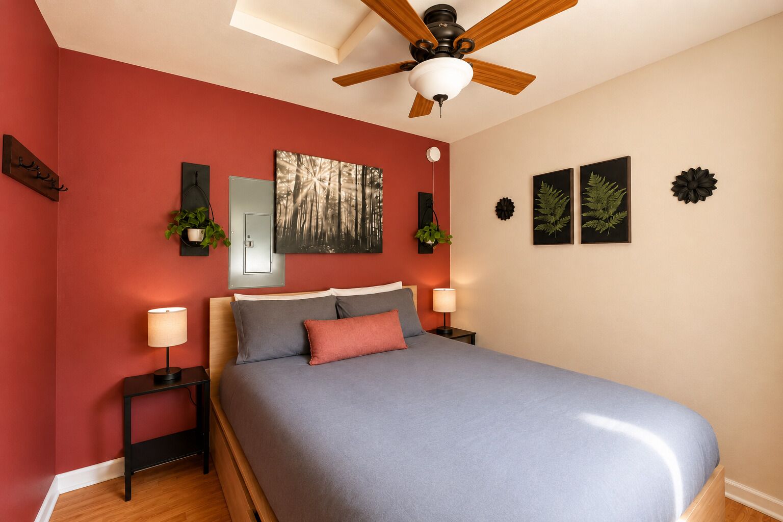 A bedroom with a bed, a ceiling fan, a nightstand with a lamp, a wall-mounted mirror, and framed botanical prints.