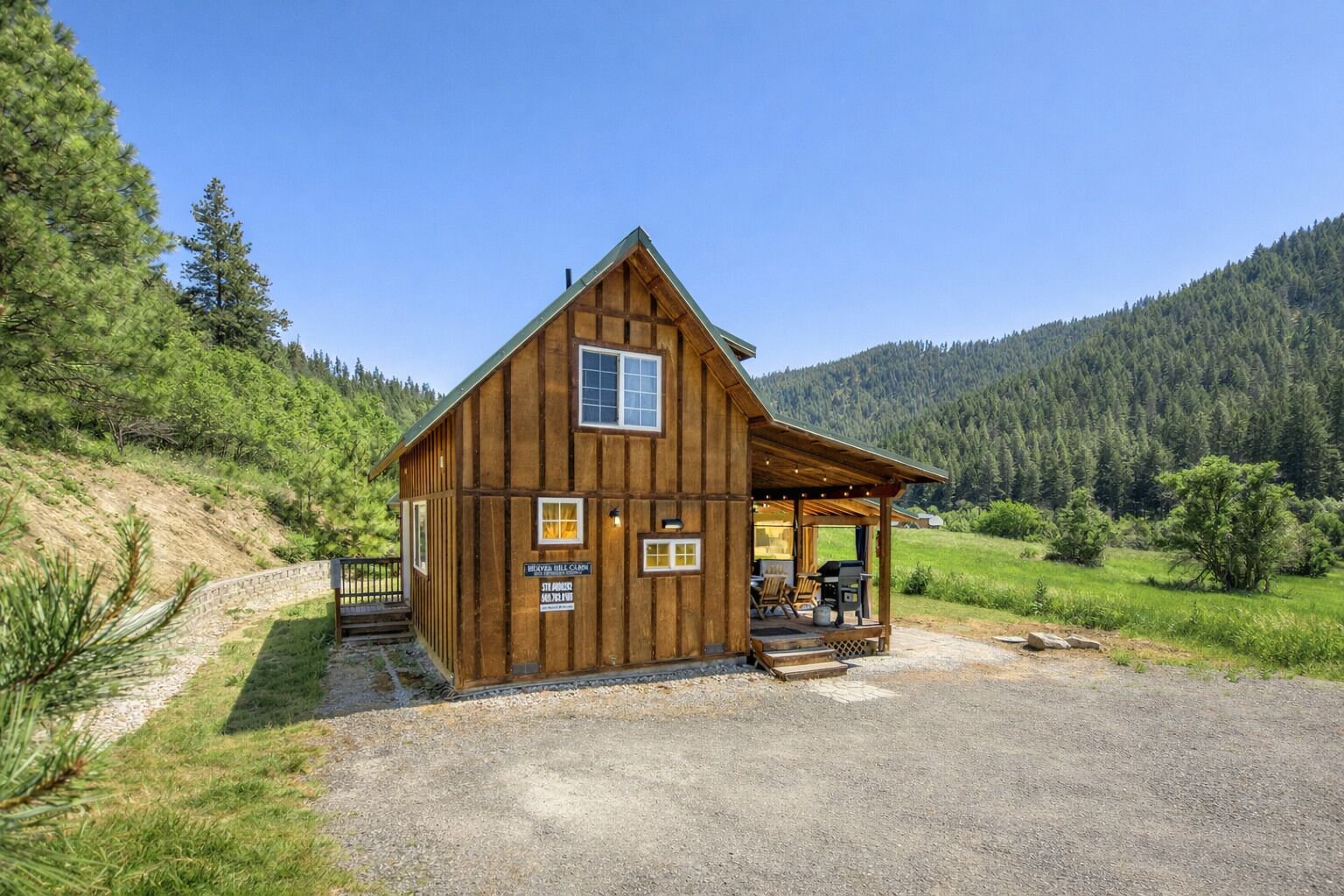 A wooden cabin with a porch, surrounded by a forested landscape.