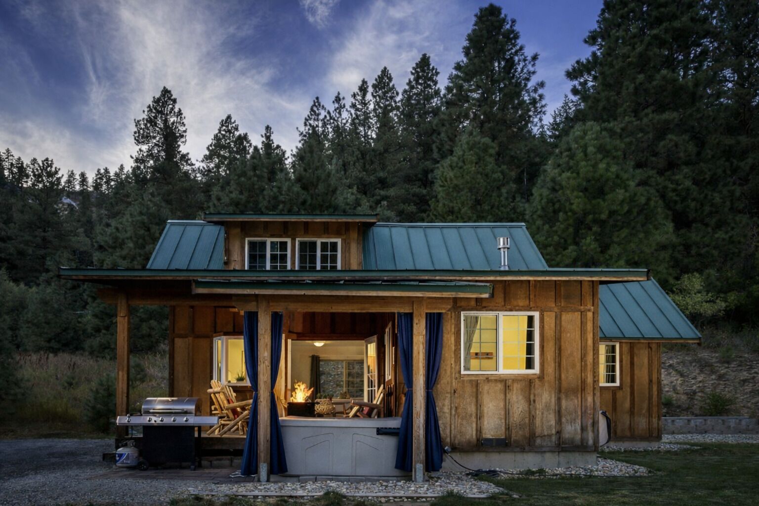 Eine rustikale Holzhütte mit überdachter Veranda, Grill und Blick auf einen bewaldeten Bereich.