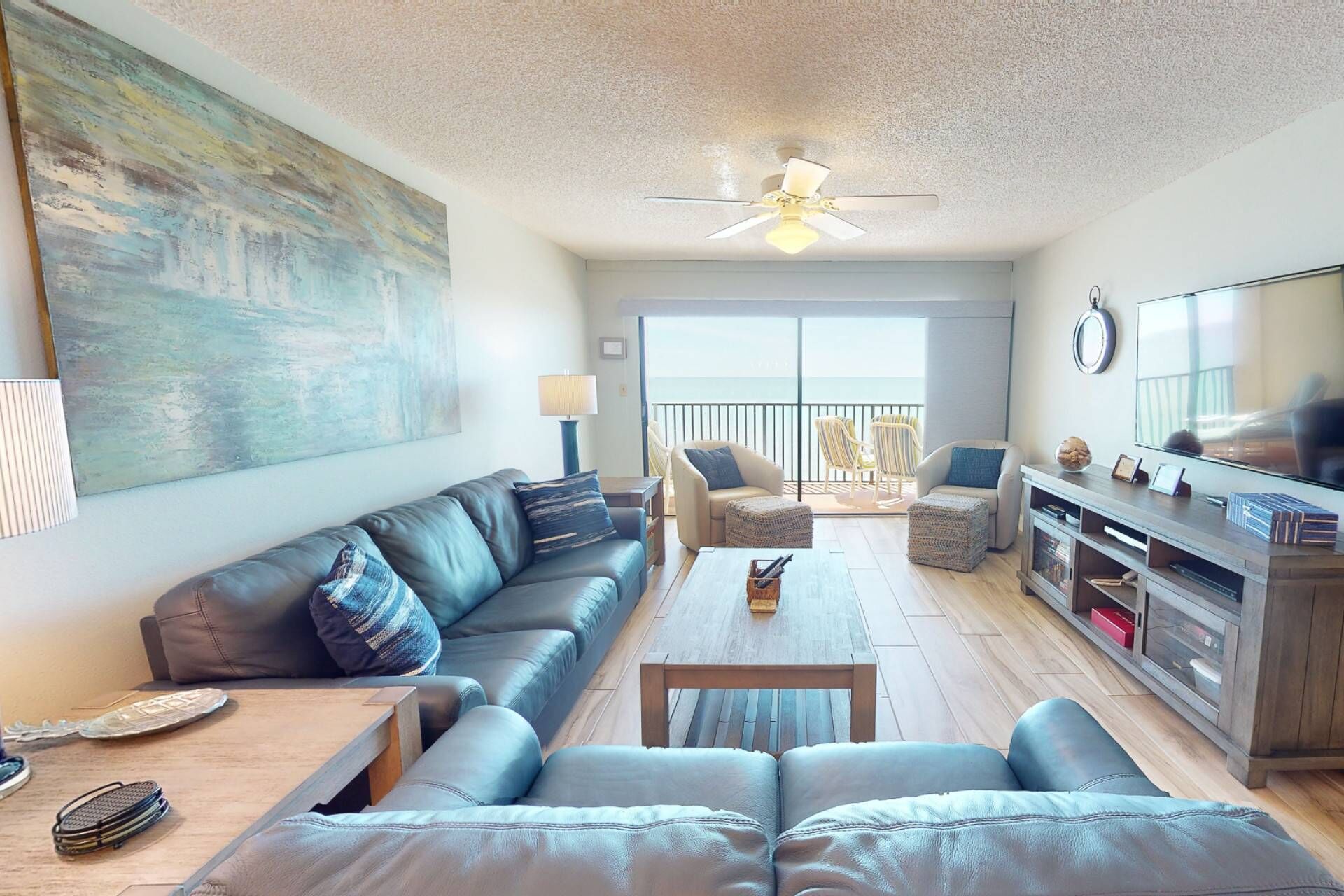 A living room with a sofa, coffee table, and chairs, a TV, and a balcony with a view.
