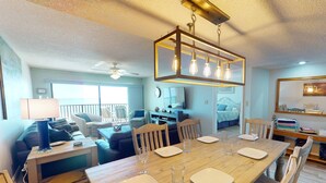 Un vaste espace de vie comprenant un coin repas avec une table pour quatre personnes, un téléviseur et un balcon aménagé avec des sièges d’extérieur.