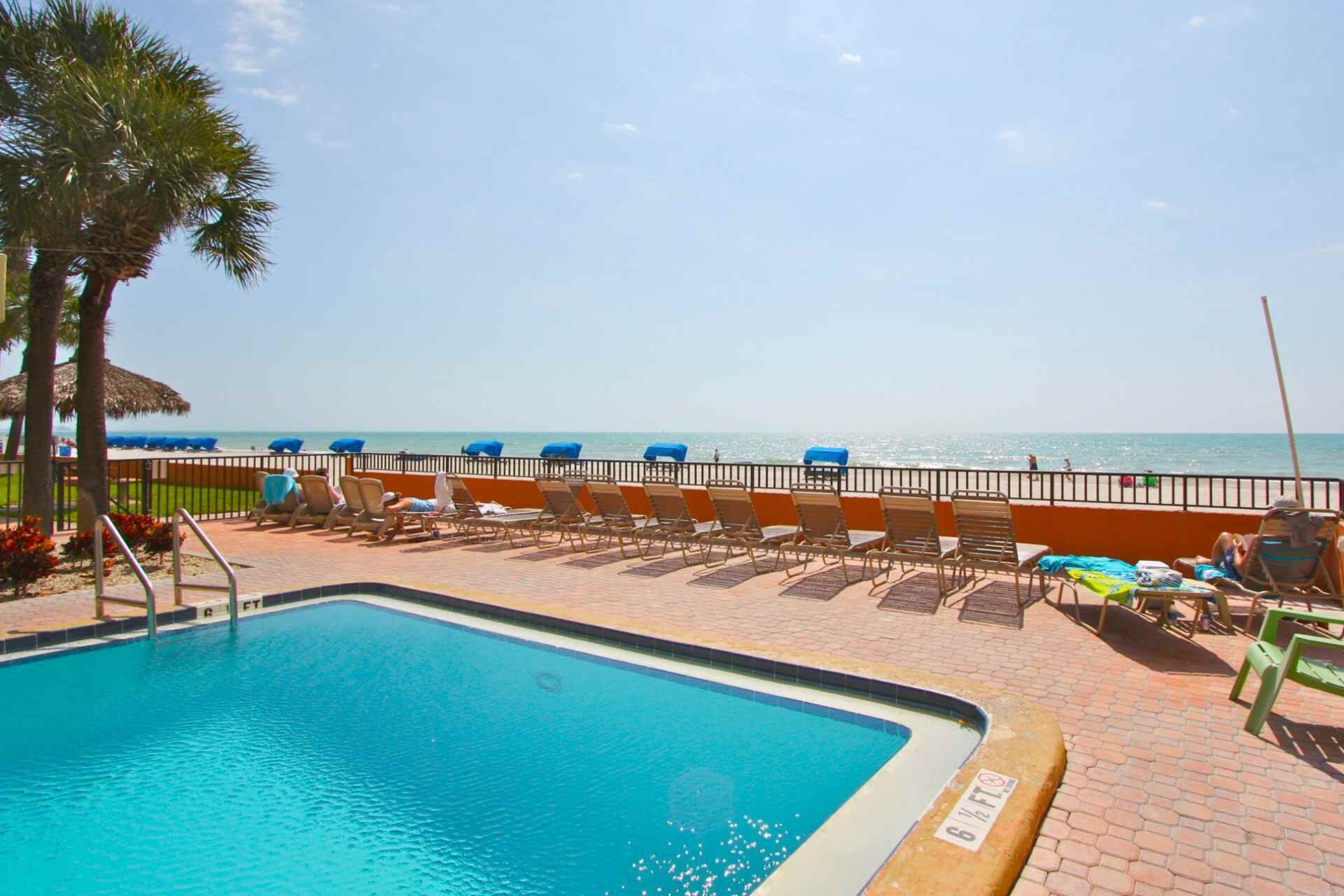 A pool area with lounge chairs and a view of the beach.