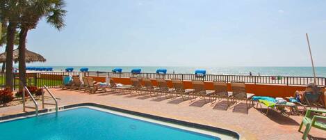 A pool area with lounge chairs and a view of the beach.