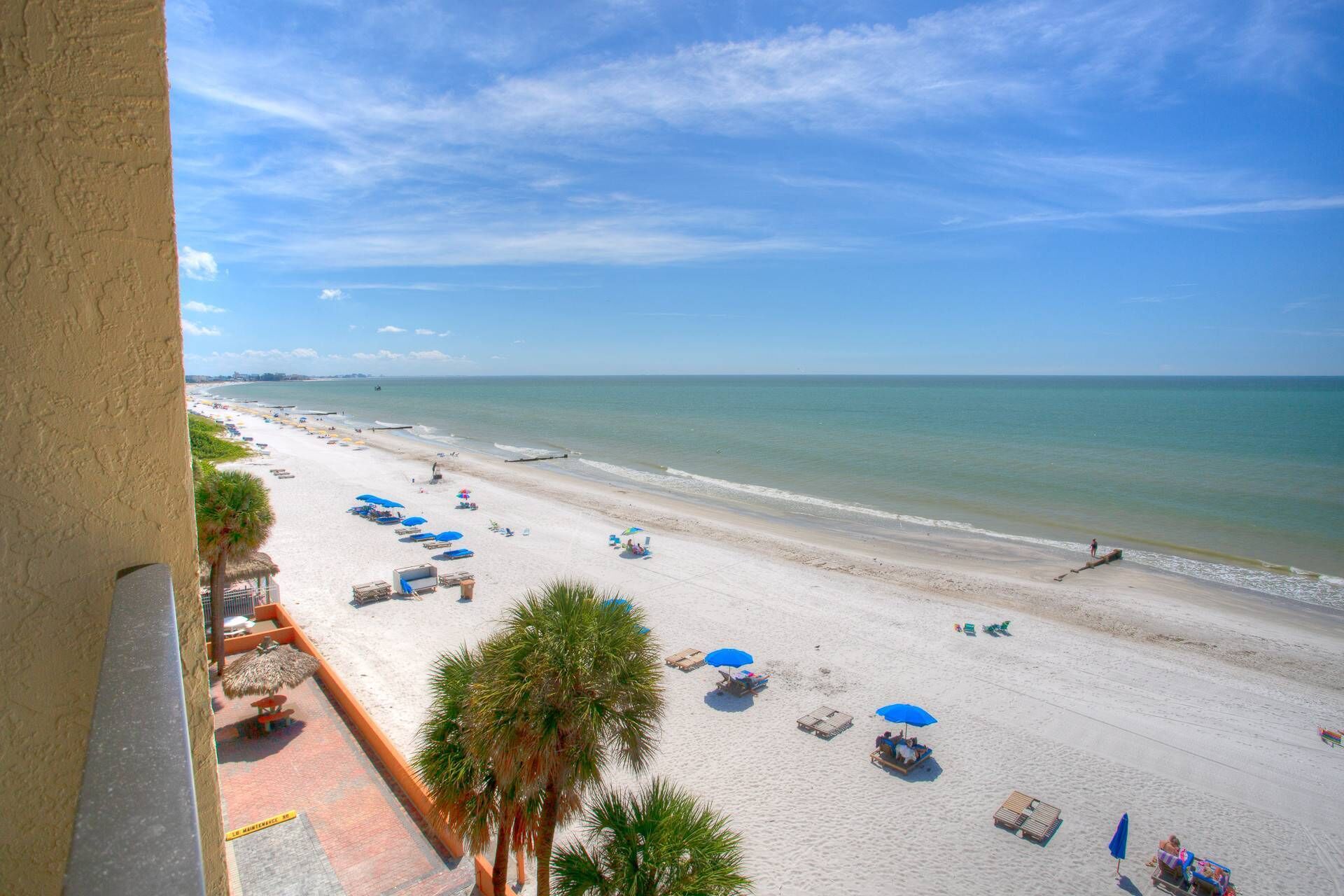 A beach with white sand, blue umbrellas, and palm trees.