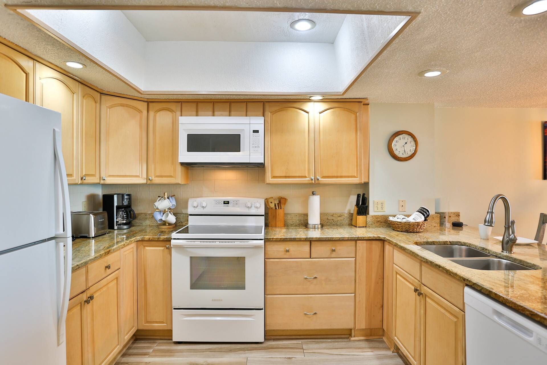 A kitchen with wooden cabinets, a microwave, a stove, a sink, and a clock on the wall.