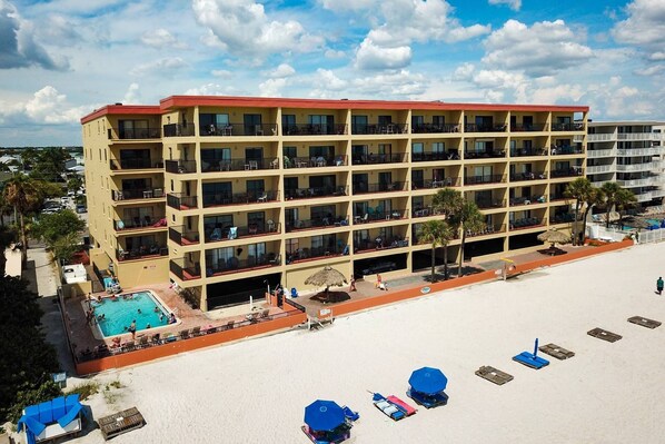Un hotel de varios pisos con balcones, piscina y zona de playa con tumbonas.