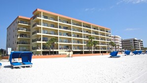 Et hotel med flere etager, altaner, en sandstrand foran og blå liggestole.
