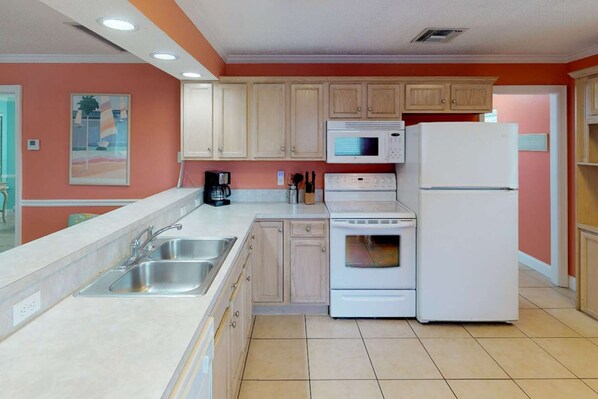 A kitchen with white appliances, beige cabinets, and a tiled floor.