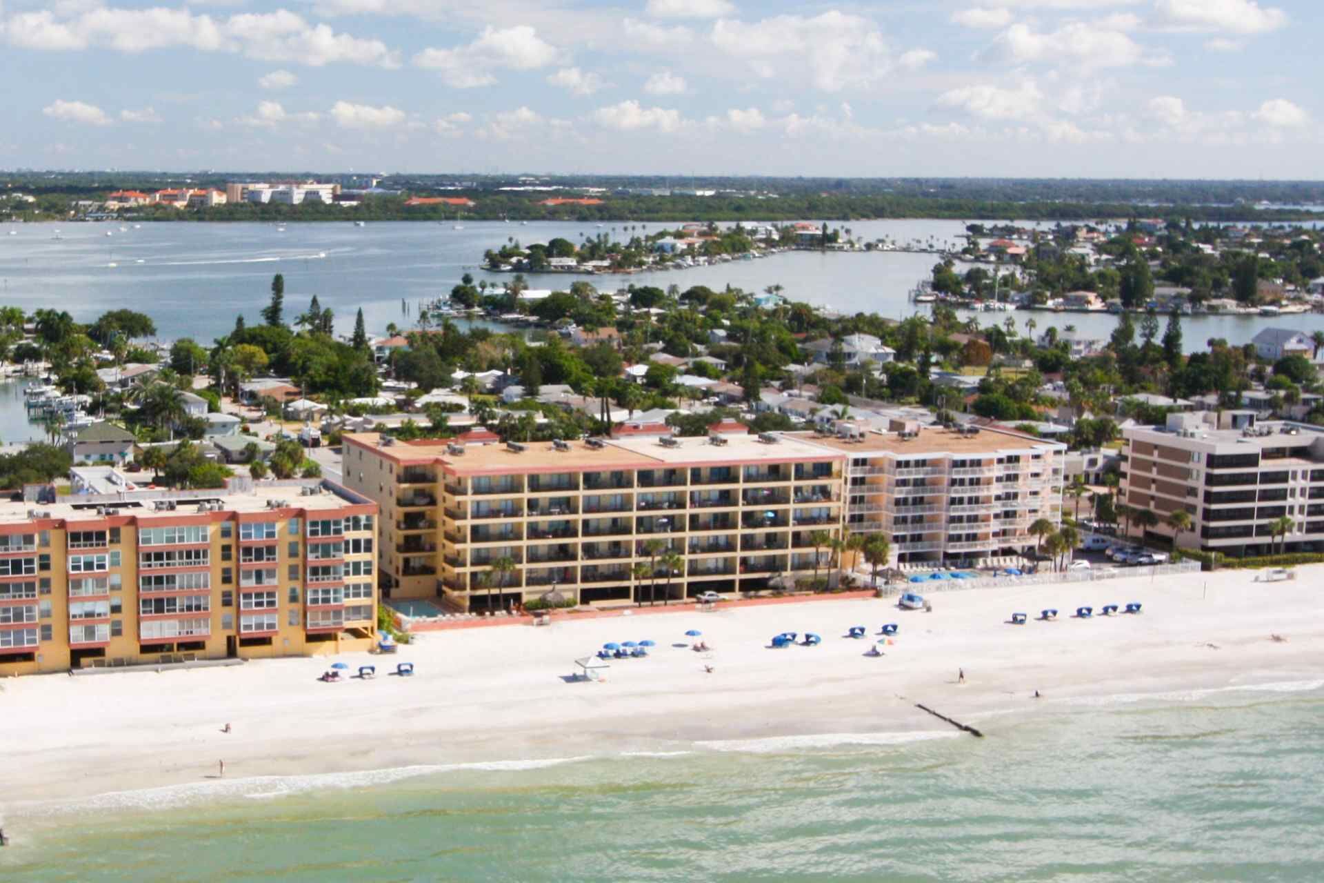 Un hotel frente a la playa con edificios de varios pisos, una playa arenosa y un puerto deportivo al fondo.