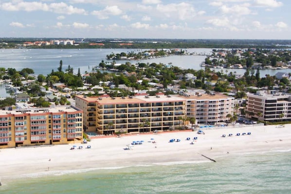 Et hotel ved stranden med flere etagers bygninger, en sandstrand og en lystbådehavn i baggrunden.