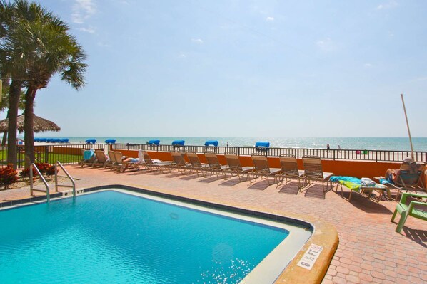 Ein Poolbereich mit Liegestühlen und Sonnenschirmen, eine Palme und Blick auf den Strand.