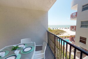 A balcony with a table set for two, overlooking a beach with a pool.