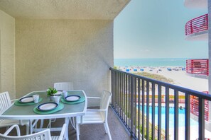 A balcony with a table set for two, overlooking a beach and a pool.