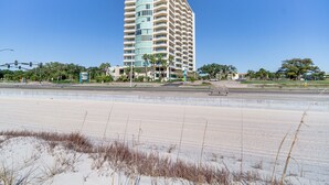 A tall, multi-story hotel with a curved facade, located near a beach with sand dunes and sparse vegetation. - Beachside Biloxi Club Condo: Balcony w/ Ocean View (Biloxi)