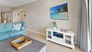 A living room with a sofa, a coffee table with a basket, a TV on a white stand, and a painting of a beach scene. - Unwind Together with a Beachfront View, Beach, Pool. 6th Floor. Tickets to Top Attractions Daily (Madeira Beach)