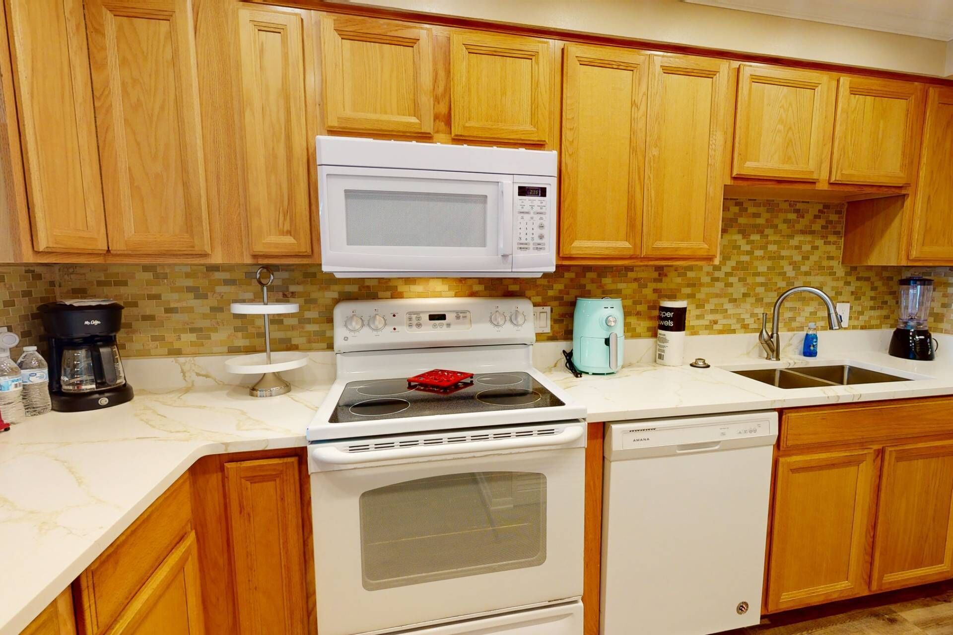 A kitchen with wooden cabinets, a white microwave, a stove, a dishwasher, and a coffee maker.