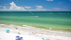 A beach with clear turquoise water, a jet ski, and a parasail in the distance. - Unwind Together with a Beachfront View, Beach, Pool. 6th Floor. Tickets to Top Attractions Daily (Madeira Beach)