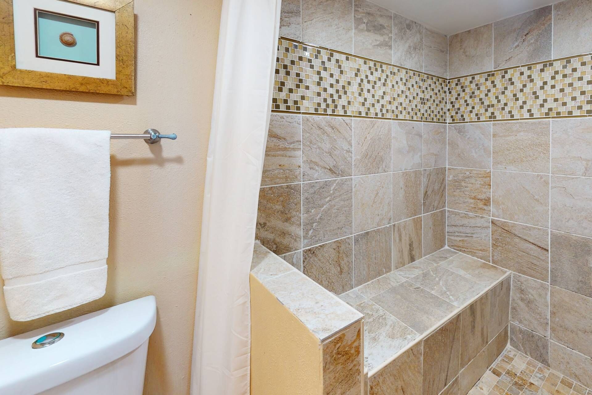 A bathroom with a toilet, a shower with tiled walls, and a framed picture on the wall.