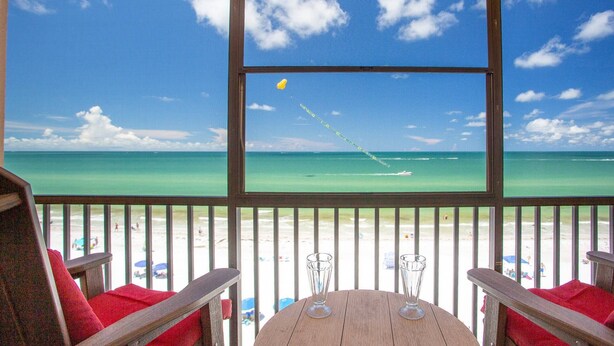 A beach view from a covered area with a table and chairs, a clear sky, and a distant boat. - Unwind Together with a Beachfront View, Beach, Pool. 6th Floor. Tickets to Top Attractions Daily (Madeira Beach)