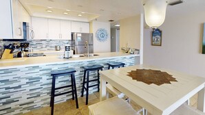 A modern kitchen with a central island, bar stools, a clock, and a decorative wall piece. - Incredible Beachfront View Private Balcony! 2 King Bedrooms, Pool & Hot Tub. Quiet and Relaxing Unit (Madeira Beach)