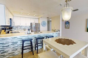 A modern kitchen with a central island, bar stools, a clock, and a decorative wall piece. - Incredible Beachfront View Private Balcony! 2 King Bedrooms, Pool & Hot Tub. Quiet and Relaxing Unit (Madeira Beach)