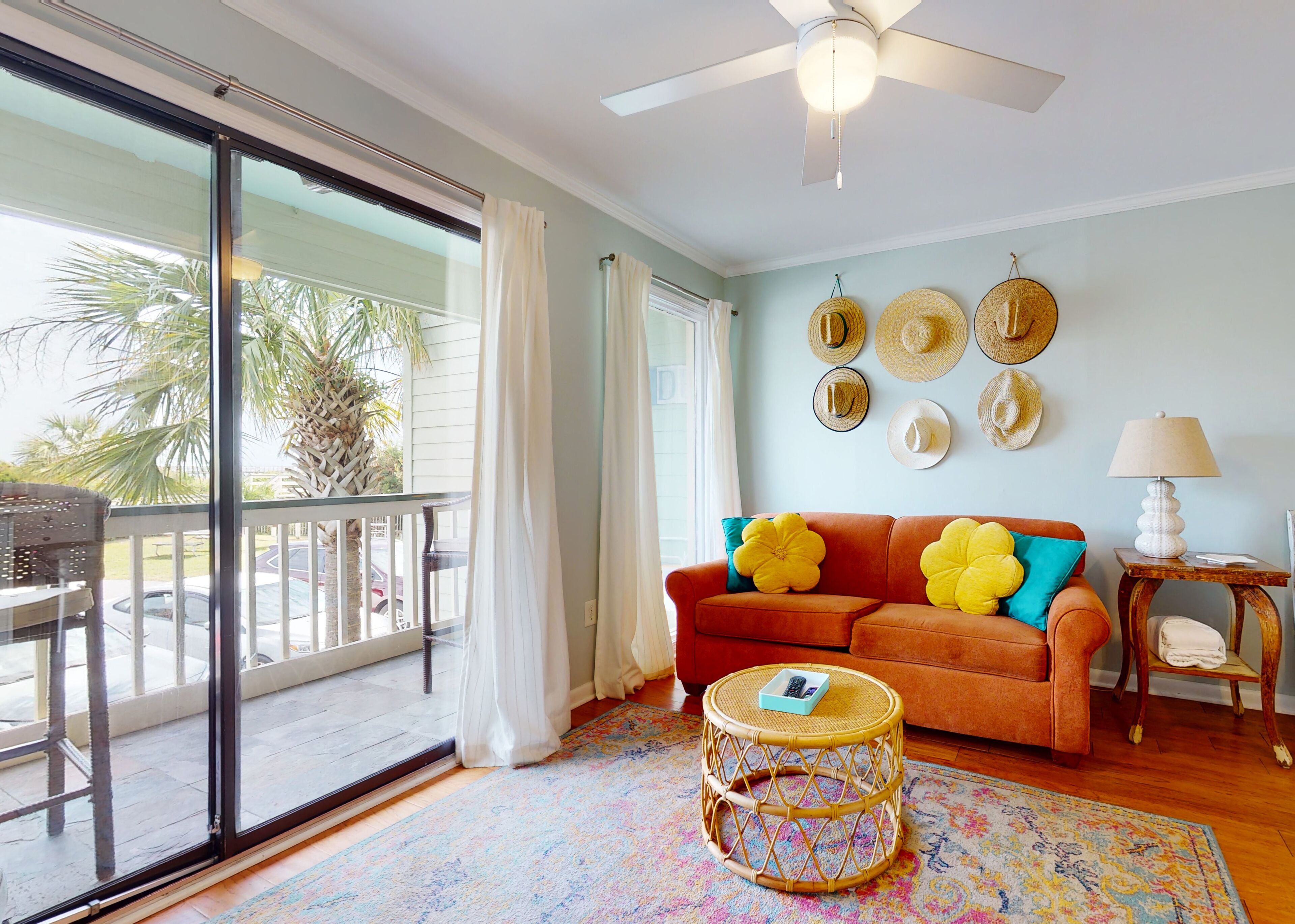 A living room with a sliding glass door, a wicker coffee table, a sofa with yellow and blue cushions, and a ceiling fan.