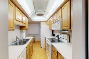 A compact kitchen with wooden cabinets, a sink, a stove, and a microwave.