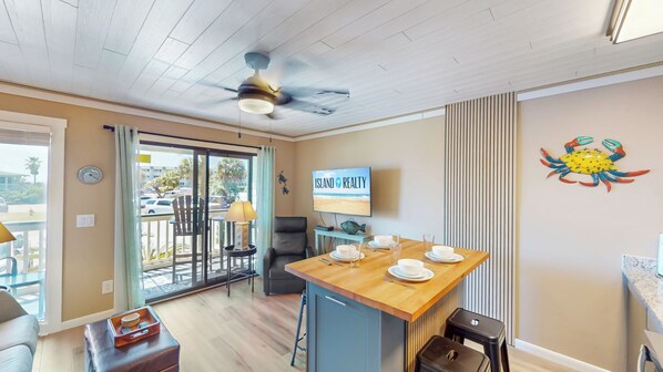 A modern kitchen with a wooden island, a ceiling fan, and a TV displaying 'Island Realty'. - Great oceanfront 1st floor unit with beach, fishing pier, and pool access (Isle of Palms)