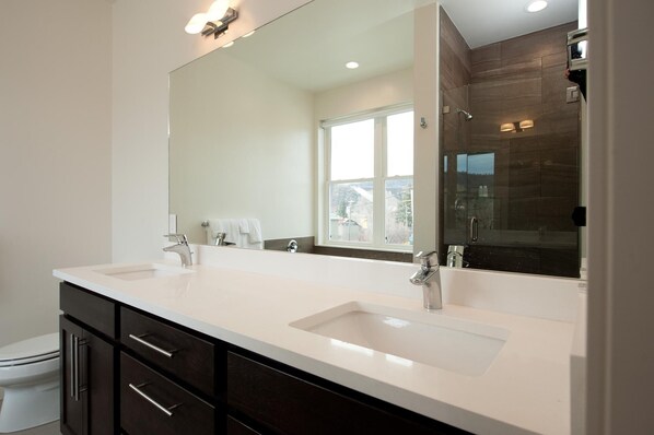 A modern bathroom with two sinks, a large mirror, and a shower area.