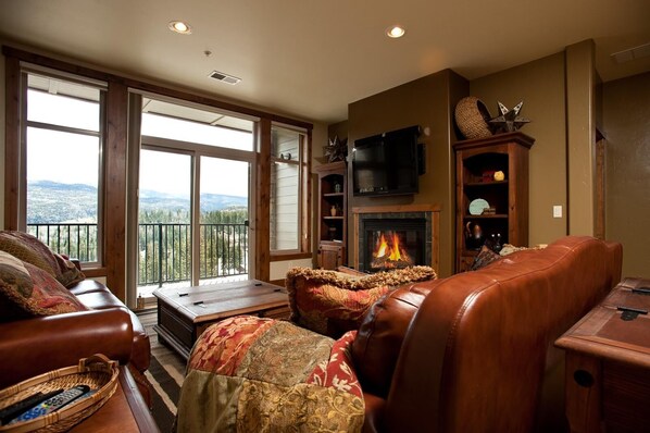 Un salón acogedor con chimenea, mobiliario de cuero y un amplio ventanal con vistas panorámicas.