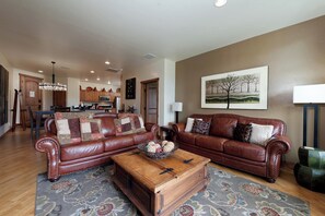 A spacious living room with leather sofas, a wooden coffee table, and a dining area with wooden cabinets and a chandelier.