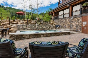 An outdoor pool area with stone walls, a hot tub, and outdoor seating.