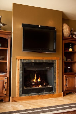 Una sala de estar con chimenea, televisor montado y muebles de madera.