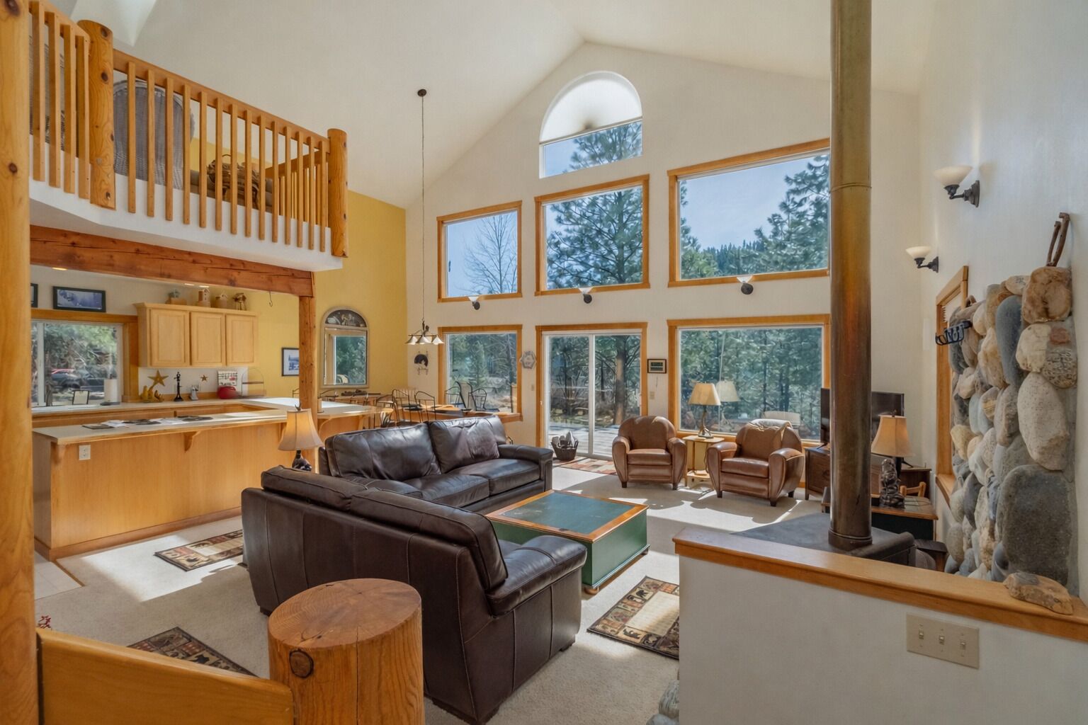A spacious living area with a high ceiling, a wooden staircase, and a kitchen area with large windows.